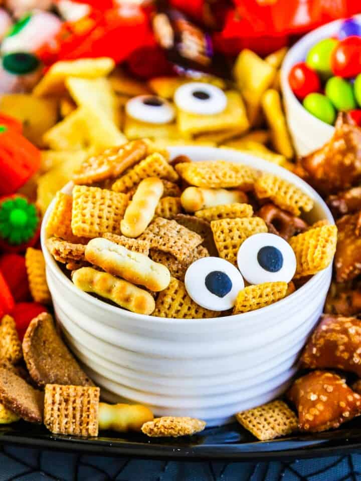 A small white bowl with chex mix and two candy eyeballs for a Halloween Snack.