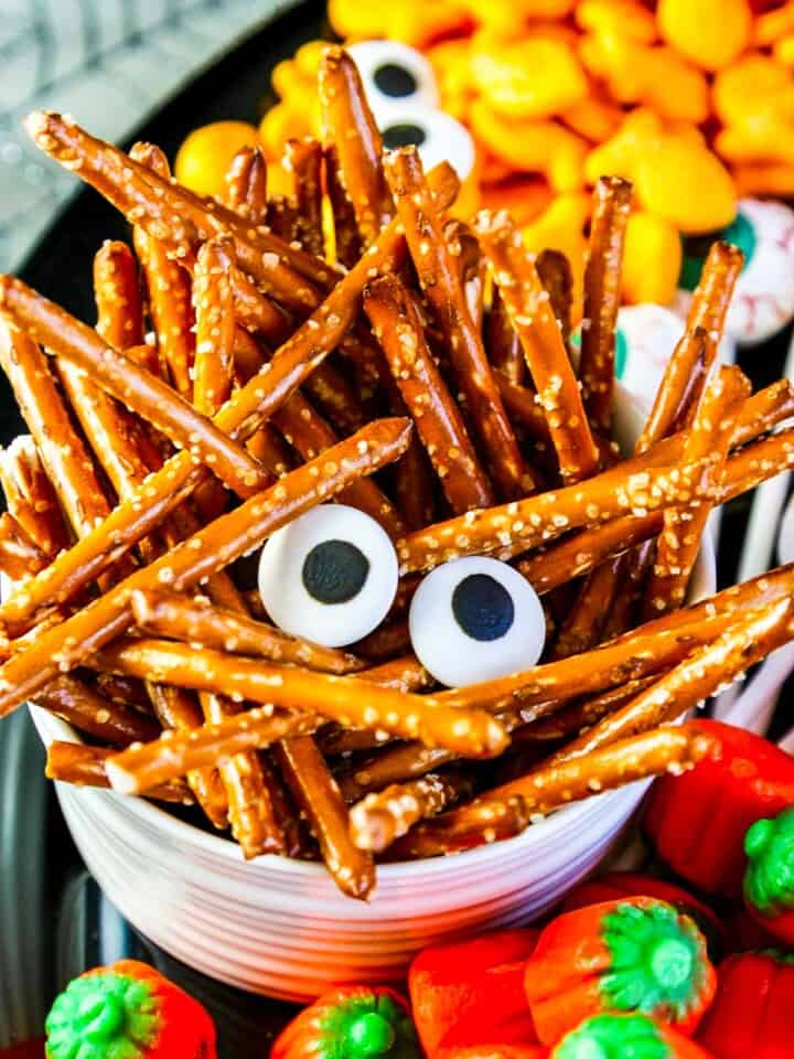 Pretzel sticks piled into a small white bowl with candy eyes for a Halloween Snack.