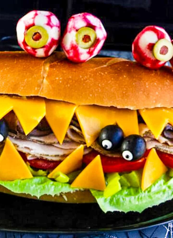 A giant sub sandwich that looks like a Monster with giant edible radish eyes and small black olive eyes.