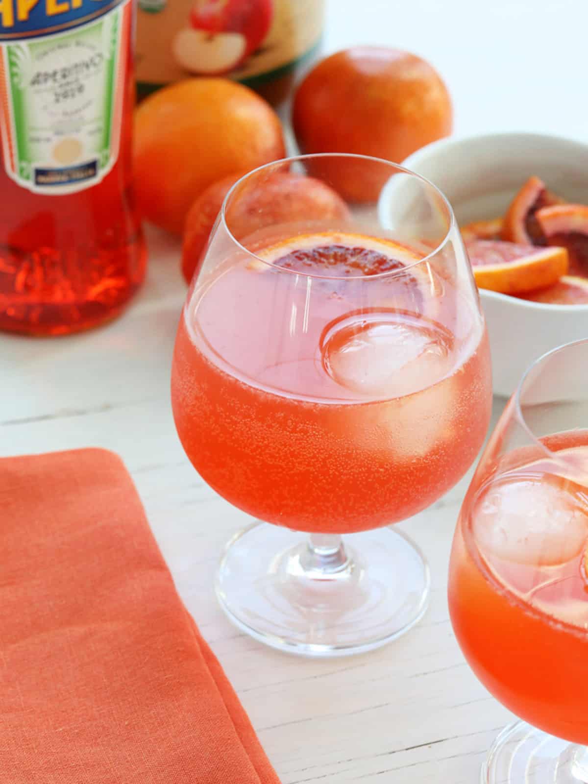 An icy cold glass of Aperol Spritz cocktail with round ice and blood orange garnish.