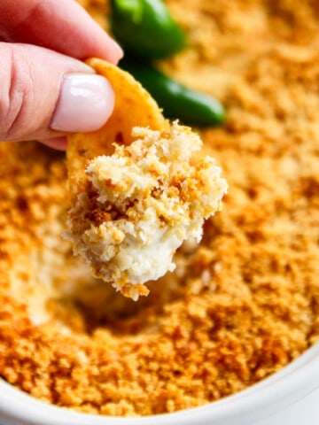 A white oval casserole dish with a hot dip being scooped out with a large corn chip.