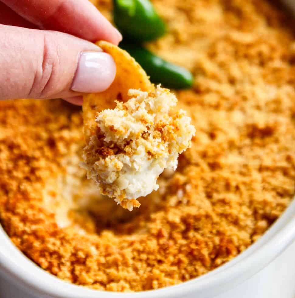 A white oval casserole dish with a hot dip being scooped out with a large corn chip.