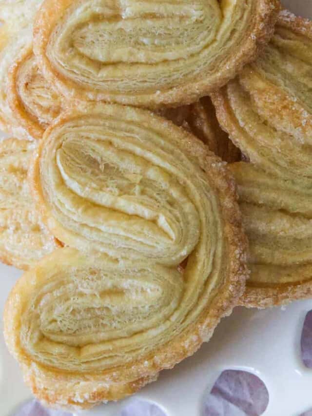 A pile of freshly baked palmier cookies on a decorative white heart plate.