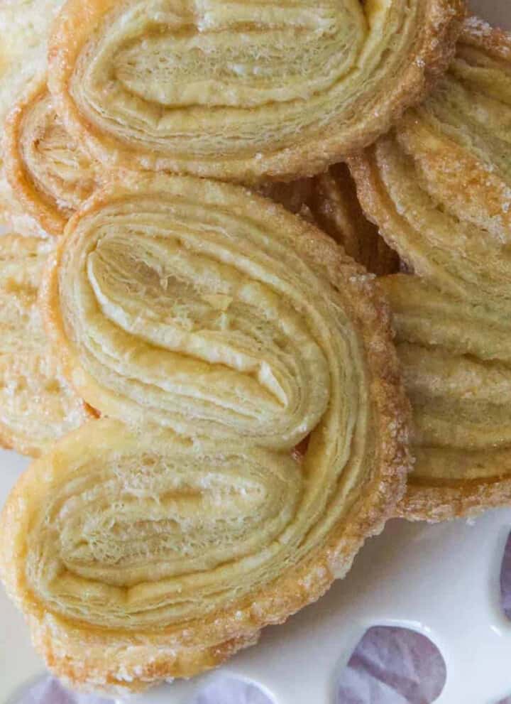 A pile of freshly baked palmier cookies on a decorative white heart plate.