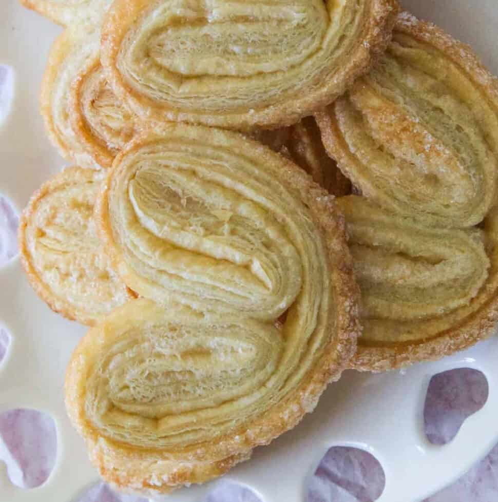 A pile of freshly baked palmier cookies on a decorative white heart plate.