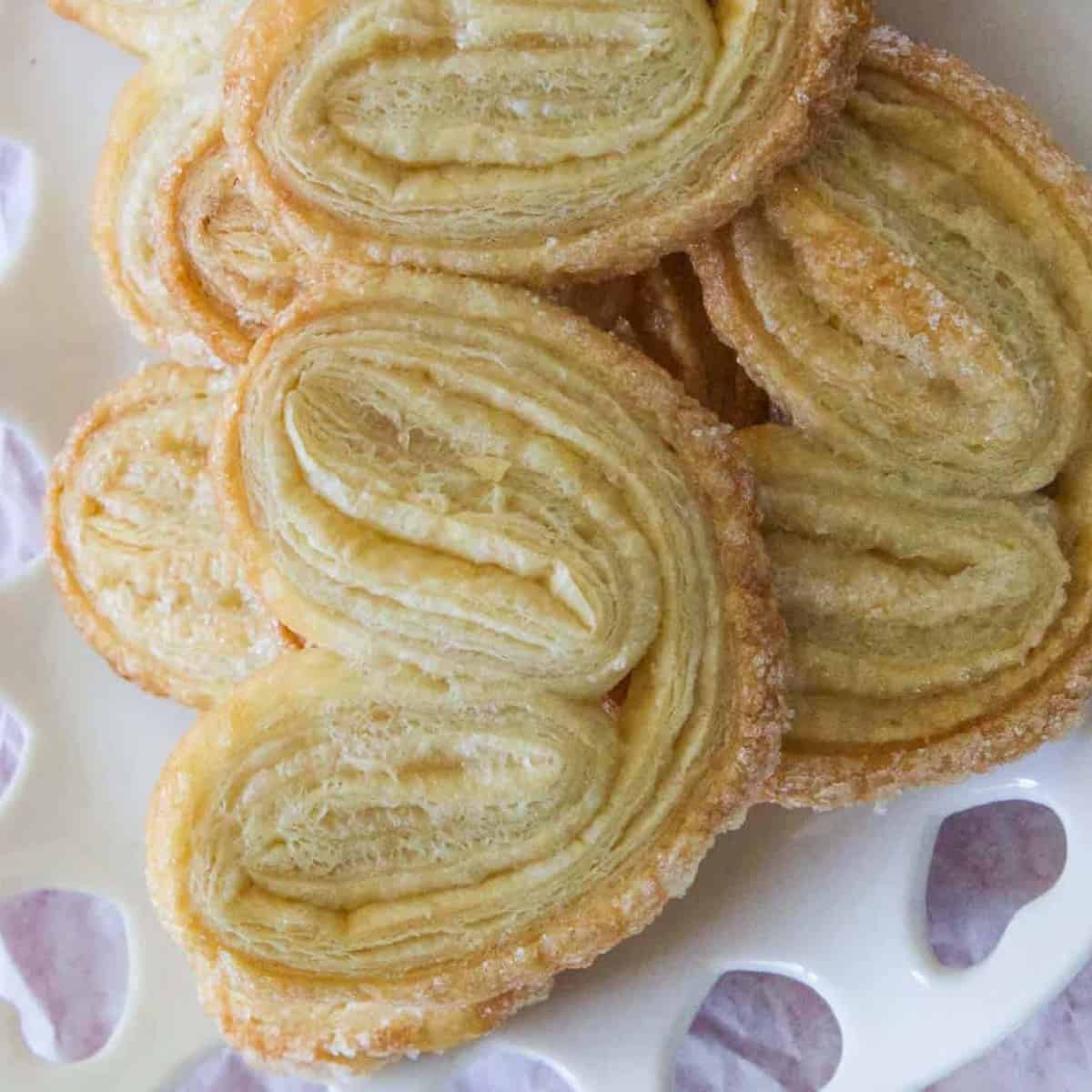 A pile of freshly baked palmier cookies on a decorative white heart plate.