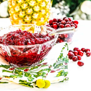 A crystal bowl filled with cranberry sauce with pineapple and cranberries in the background.