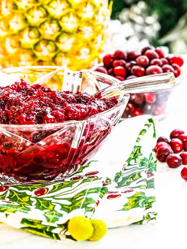 A crystal bowl filled with cranberry sauce with pineapple and cranberries in the background.