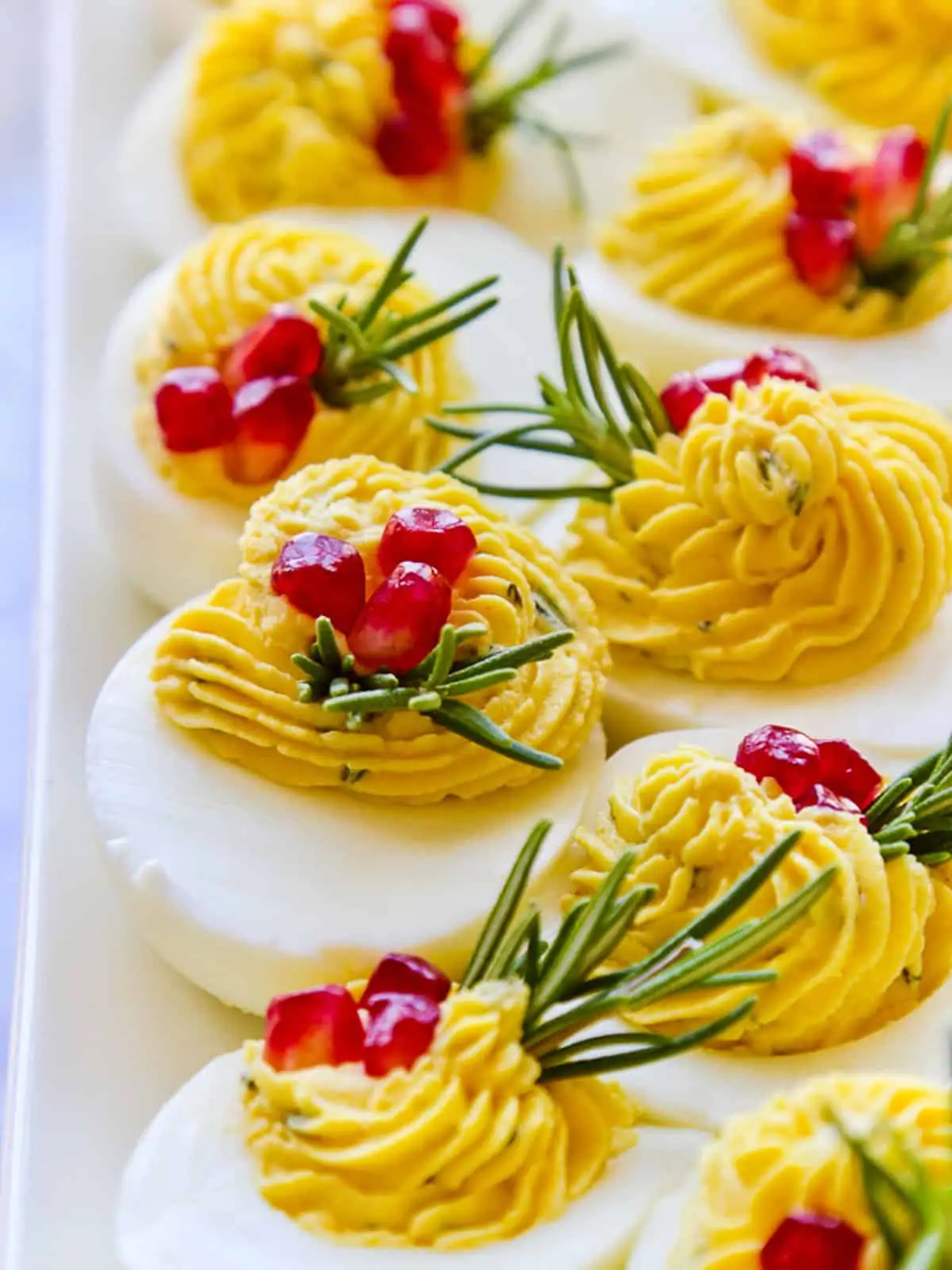 A platter of holiday Christmas deviled eggs garnished with rosemary and pomegranate seeds.