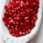 A white ceramic dish with pomegranate seeds ready to use in a recipe.