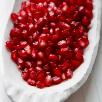 A white ceramic dish with pomegranate seeds ready to use in a recipe.