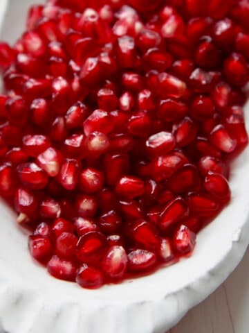 A white ceramic dish with pomegranate seeds ready to use in a recipe.
