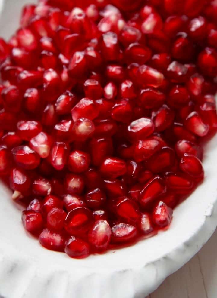 A white ceramic dish with pomegranate seeds ready to use in a recipe.