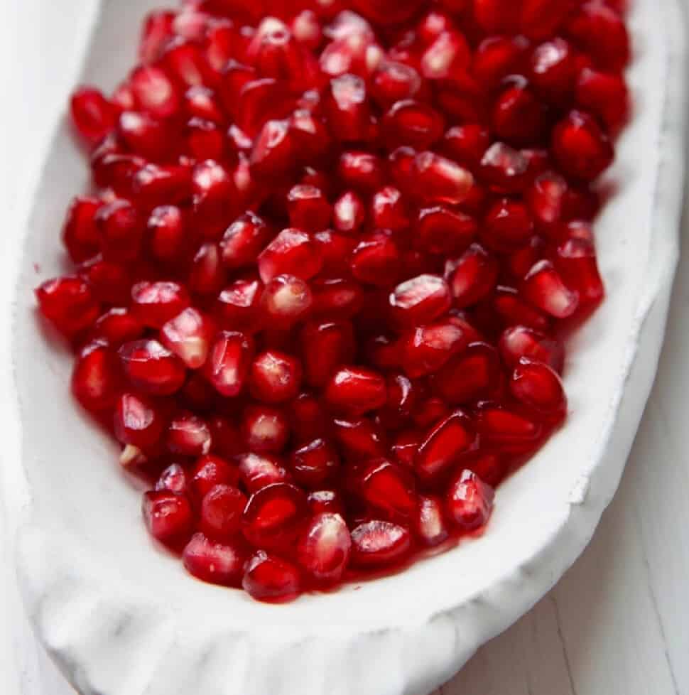 A white ceramic dish with pomegranate seeds ready to use in a recipe.