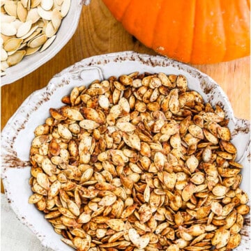 A ceramic dish full of golden brown roast pumpkin seeds.