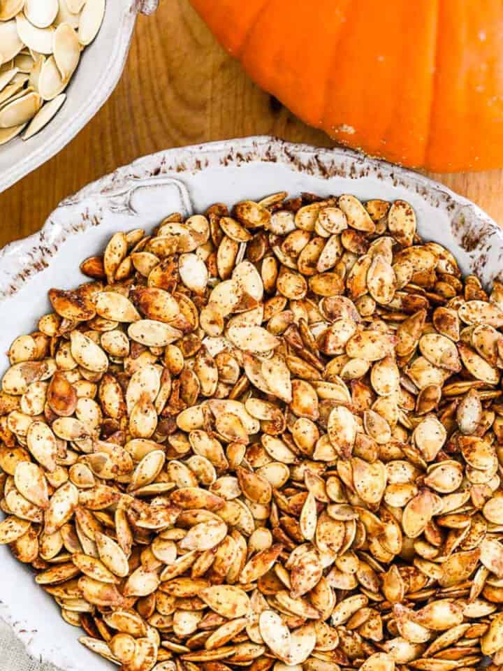 A ceramic dish full of golden brown roast pumpkin seeds.