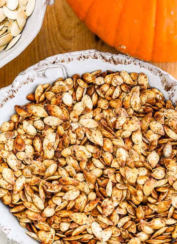 A ceramic dish full of golden brown roast pumpkin seeds.