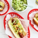 A red plastic food basket lined with paper holding a loaded grilled hot dog.