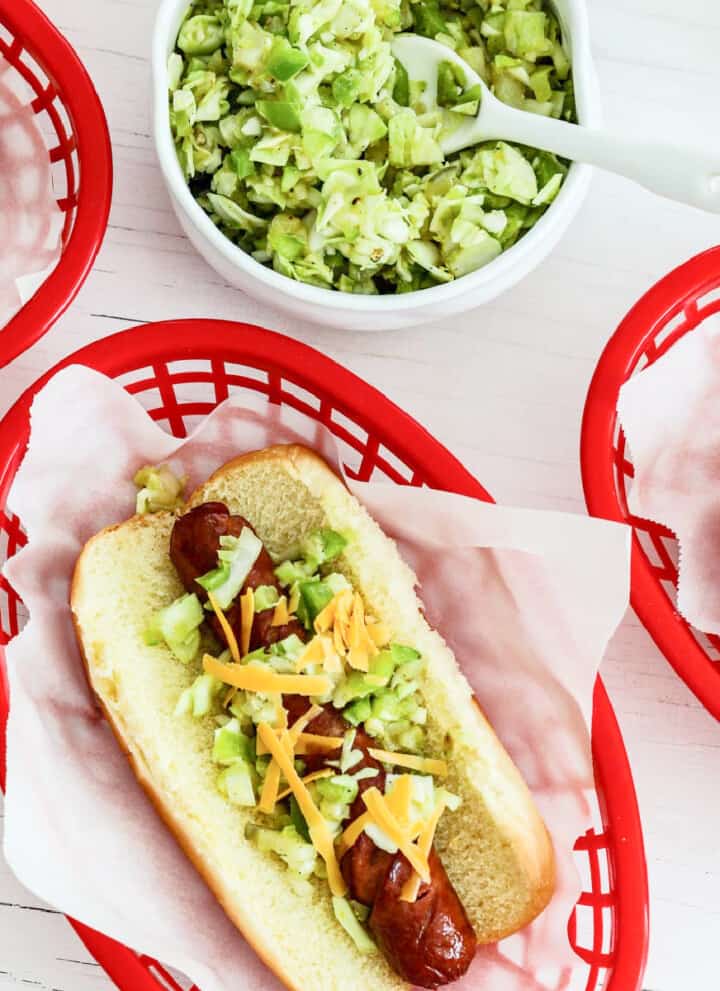 A red plastic food basket lined with paper holding a loaded grilled hot dog.