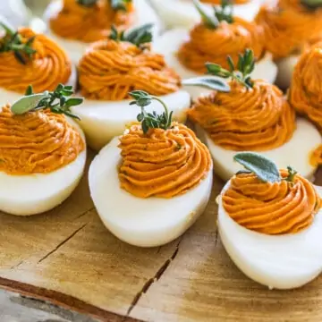 A slice of rustic tree wood with Thanksgiving deviled eggs garnished with fresh herbs.