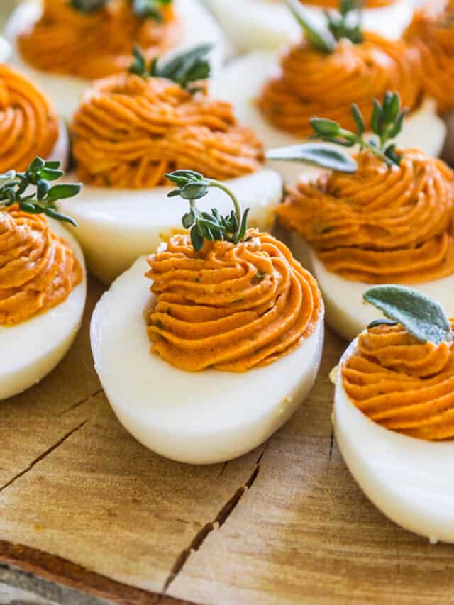 A slice of rustic tree wood with Thanksgiving deviled eggs garnished with fresh herbs.