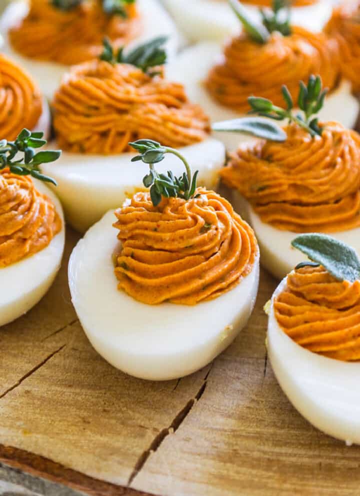 A slice of rustic tree wood with Thanksgiving deviled eggs garnished with fresh herbs.