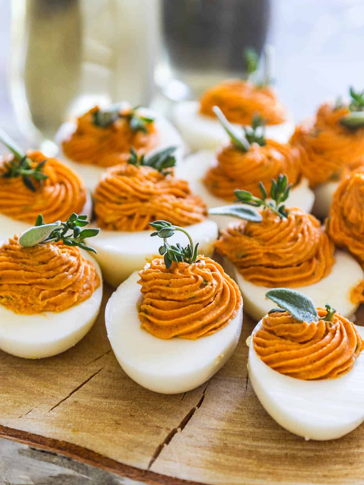 A rustic piece of tree cut into a platter with Thanksgiving deviled eggs filled with rust colored filling and garnished with herbs.