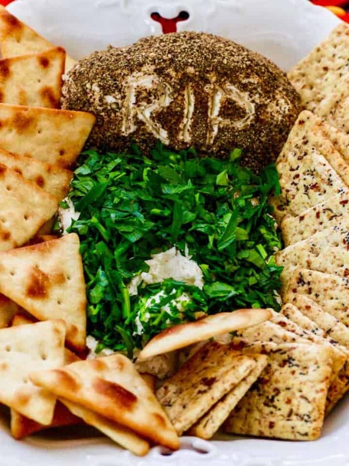 A cracker scooping out some Halloween dip shaped like a tombstone in a white dish.