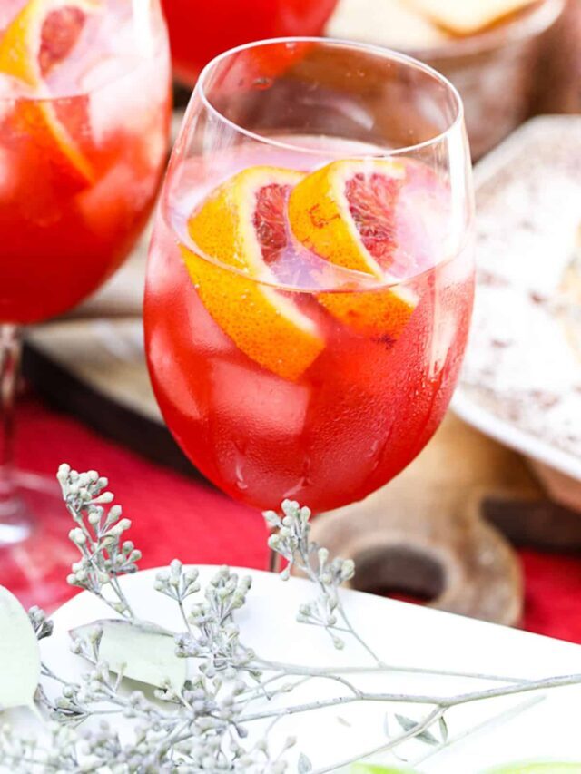 A wine glass filled with Aperol Spritz cocktail garnished with blood orange slices.