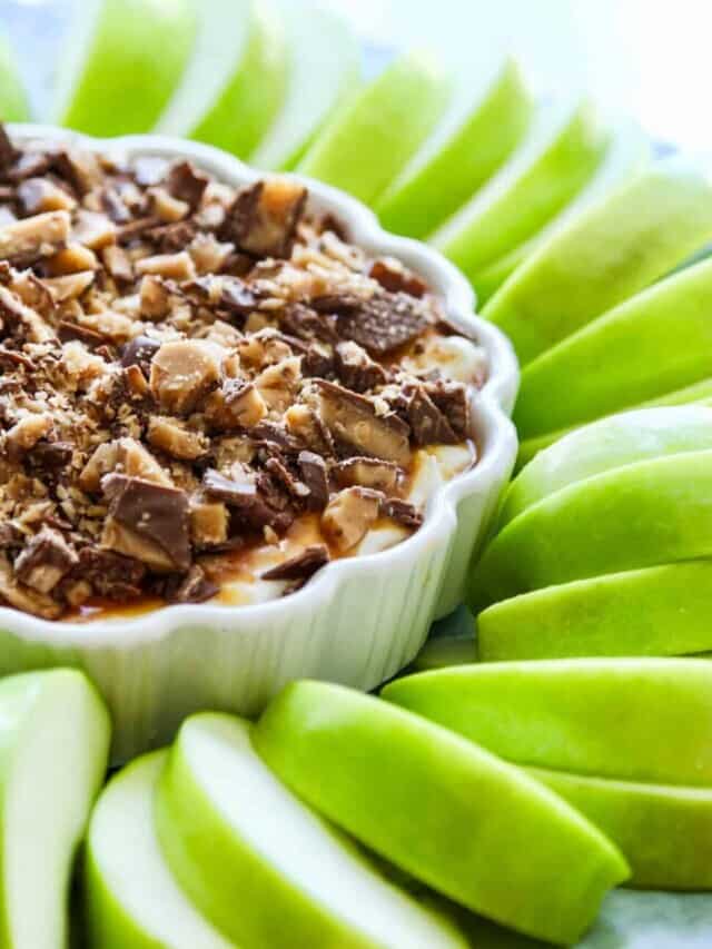 Cut green apple slices in a spiral pattern with a sweet dessert dip topped with crushed candy bars on top.