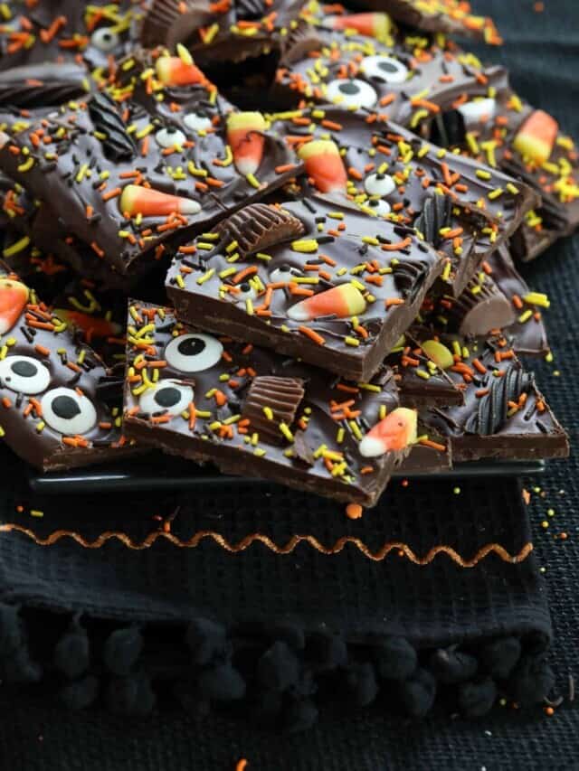 A black platter with shards of Halloween bark made with chocloate candy and sprinkles
