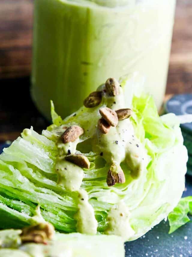 A wedge salad of iceberg lettuce with a drizzle of avocado dressing and topped with crushed pistachios, and a large mason jar of the dressing on the black board.