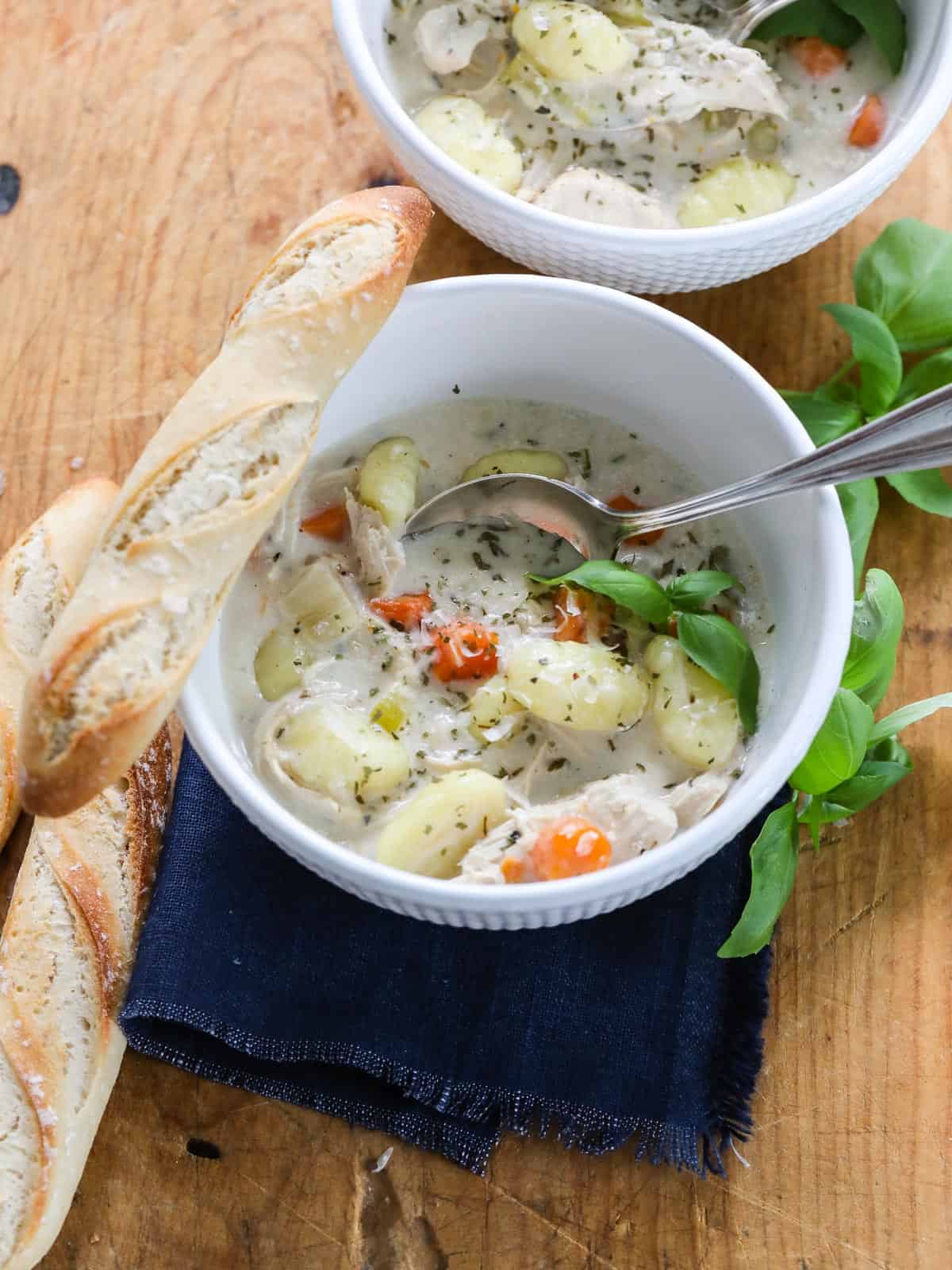 A bowl of Chicken Gnocchi Soup and a small baguette on the edge of the bowl.