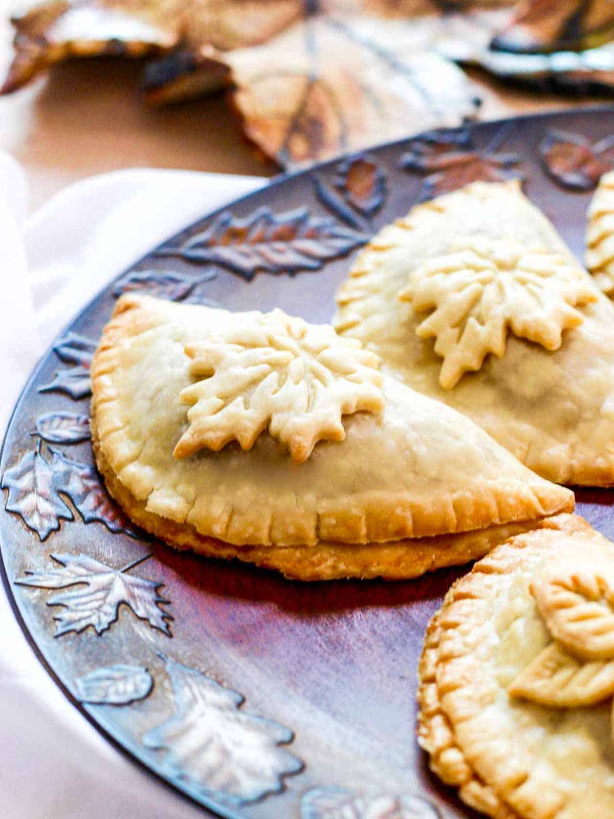Golden brown baked empanadas decorated with pie crust leaves on a Fall tray.
