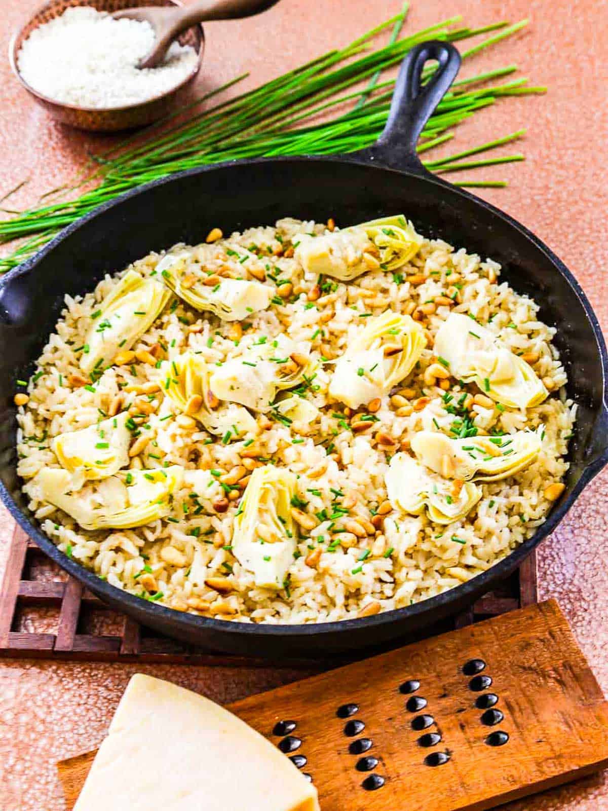 A pan of risotto on a wood hot pad on a table.