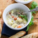 A white bowl full of Chicken Gnocchi Soup with a silver spoon and bread nearby.