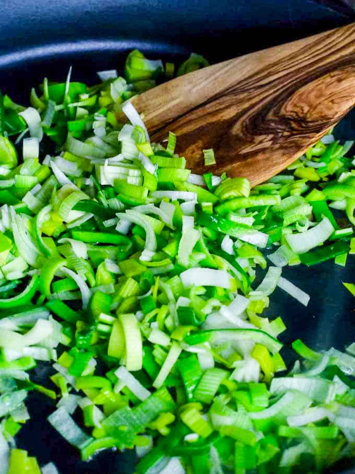 Chopped leeks stirred in a pan with an olive wood spoon.