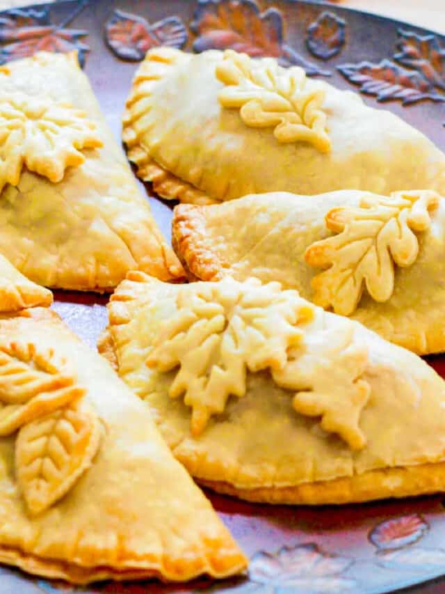 Golden brown baked empanadas decorated with pie crust leaves on a Fall tray.