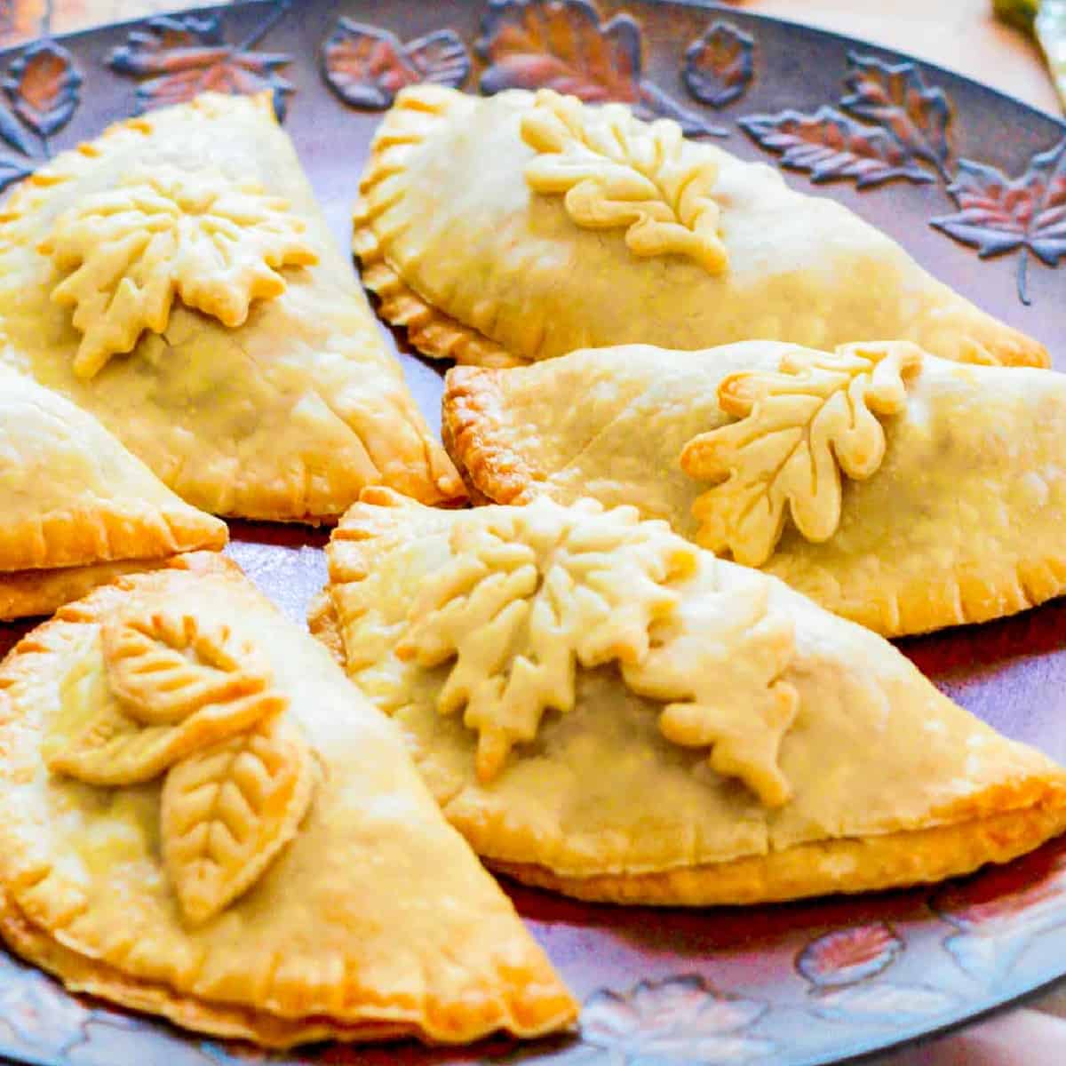 Golden brown baked empanadas decorated with pie crust leaves on a Fall tray.