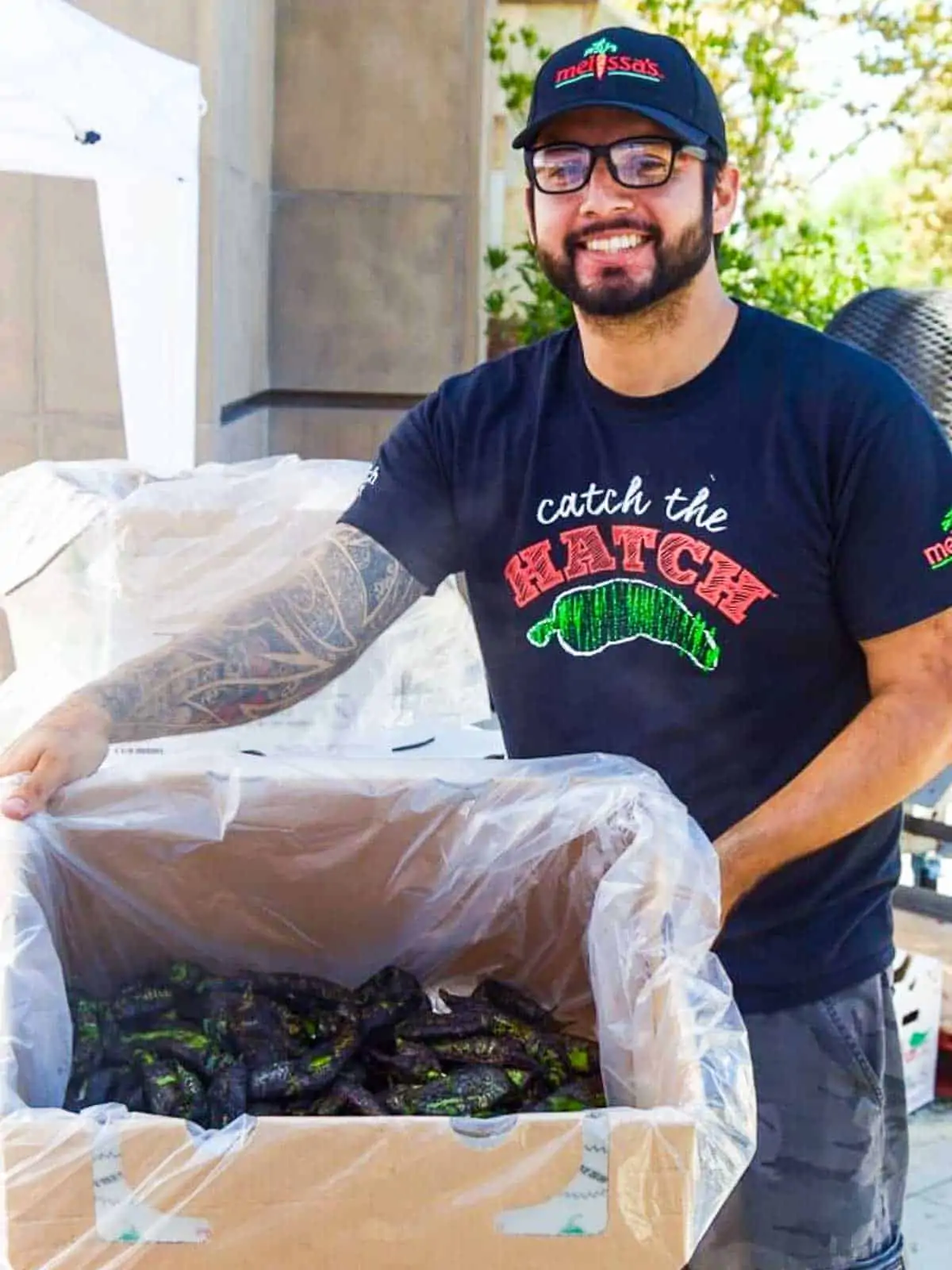 A happy smiling man holding a box of roasted Hatch Chiles in a box lined with plastic. 