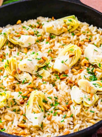 A black cast iron pan with risotto made from arborio rice topped with artichokes and pine nuts.