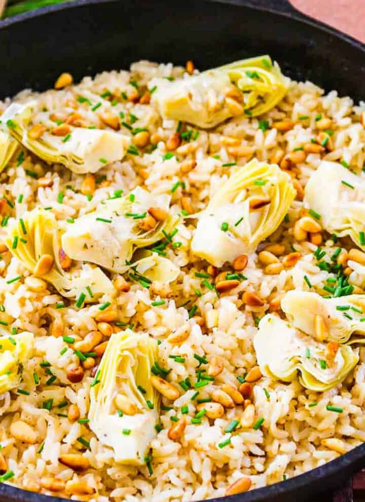 A black cast iron pan with risotto made from arborio rice topped with artichokes and pine nuts.