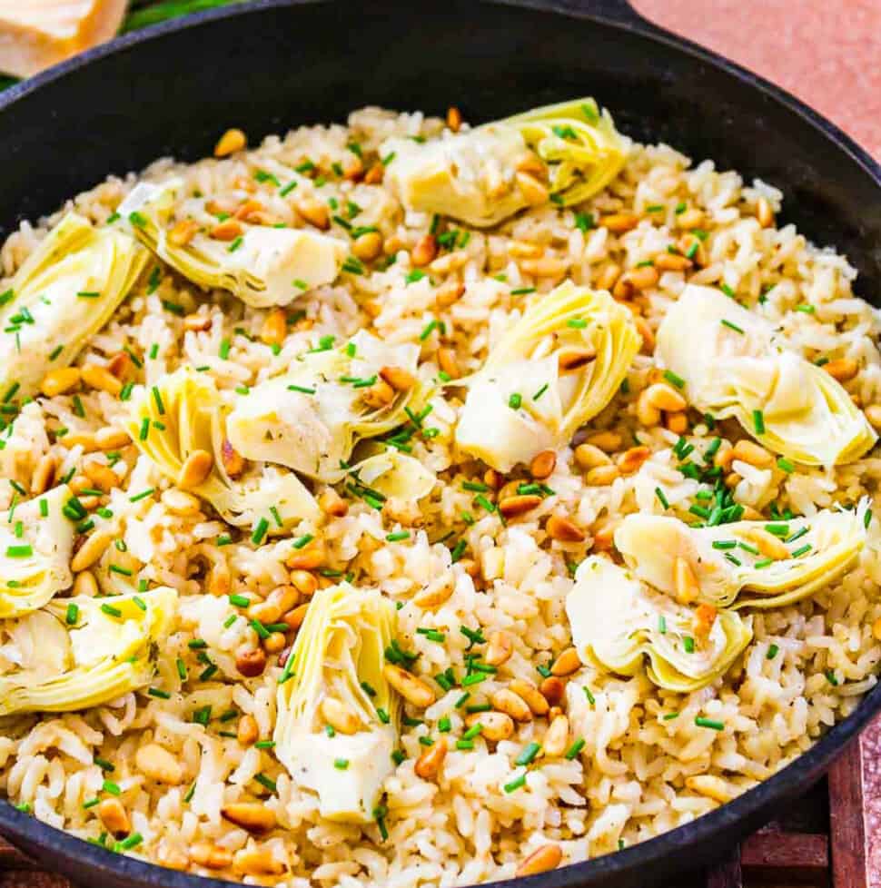 A black cast iron pan with risotto made from arborio rice topped with artichokes and pine nuts.