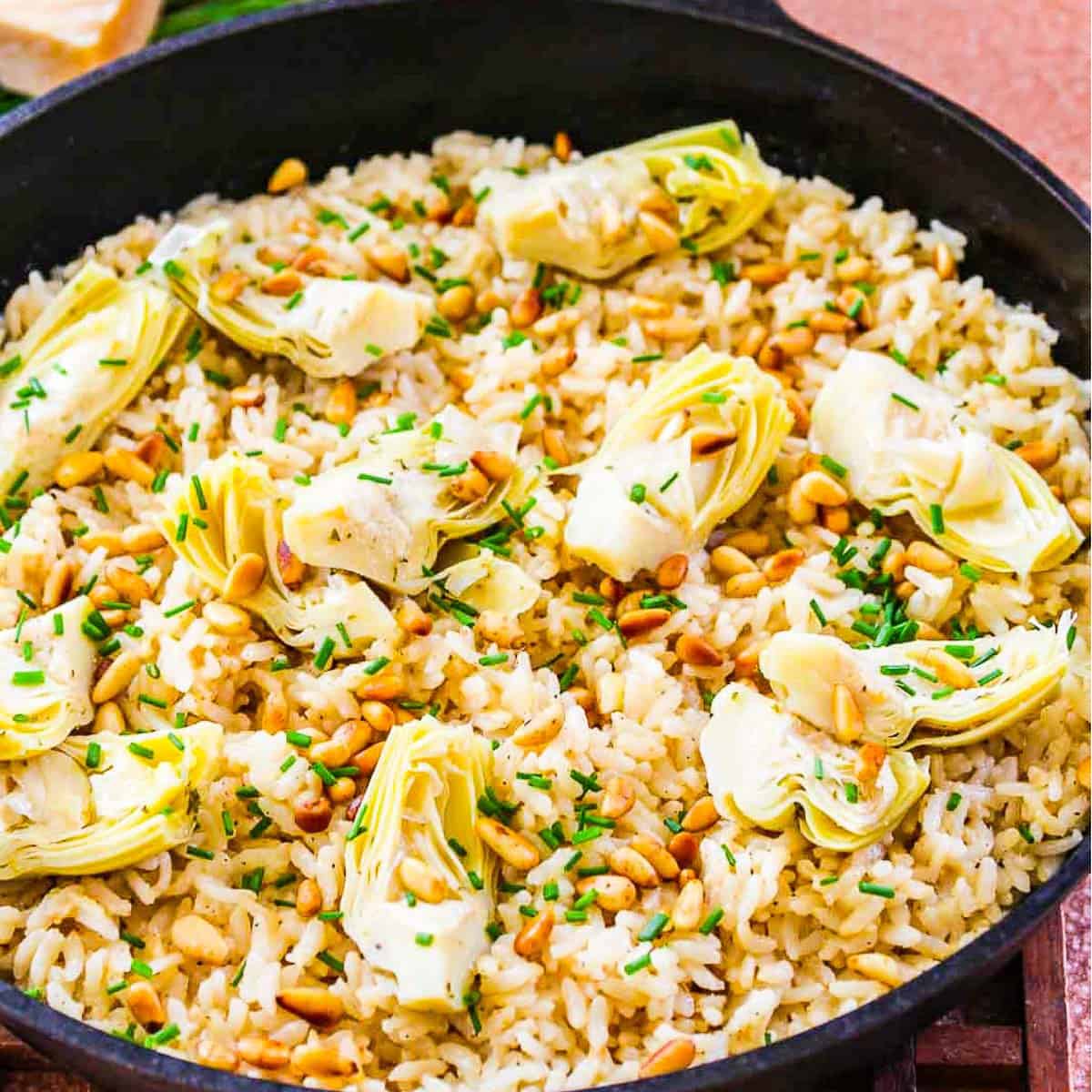 A black cast iron pan with risotto made from arborio rice topped with artichokes and pine nuts.
