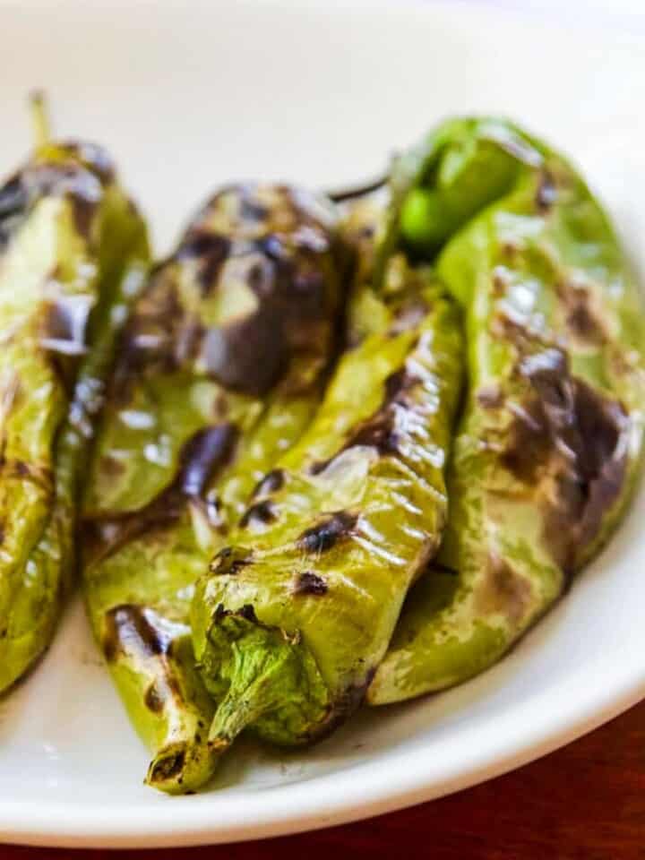 Fire roasted Hatch Chiles on a white plate ready to remove the seeds and stems.