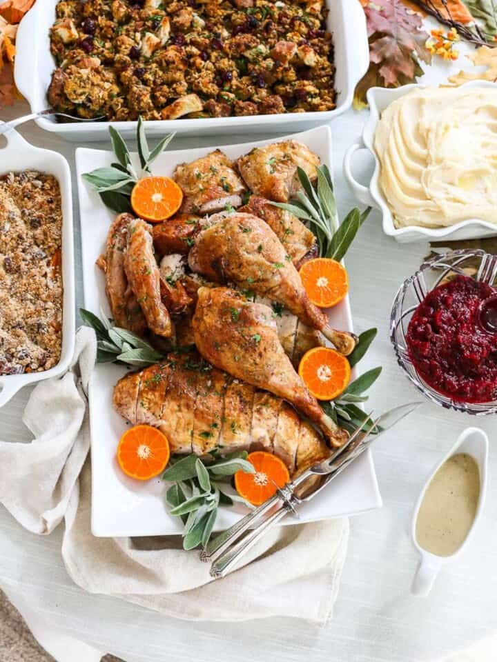 A Thanksgiving table set with a carved turkey on a platter, stuffing, mashed potatoes and gravy in white dishes.