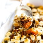 A silver server scooping up sweet potato casserole with golden toasted marshmallows on top out of a white casserole dish.