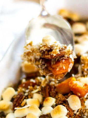 A silver server scooping up sweet potato casserole with golden toasted marshmallows on top out of a white casserole dish.