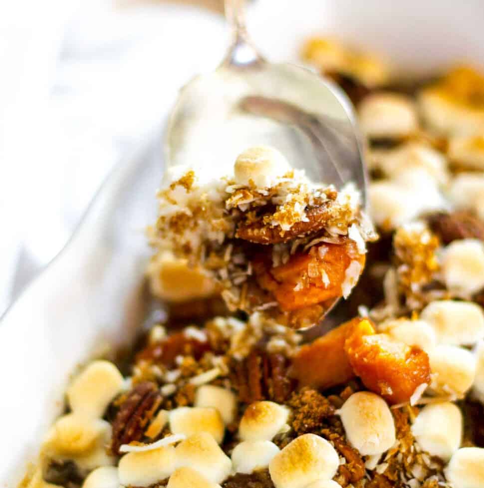 A silver server scooping up sweet potato casserole with golden toasted marshmallows on top out of a white casserole dish.