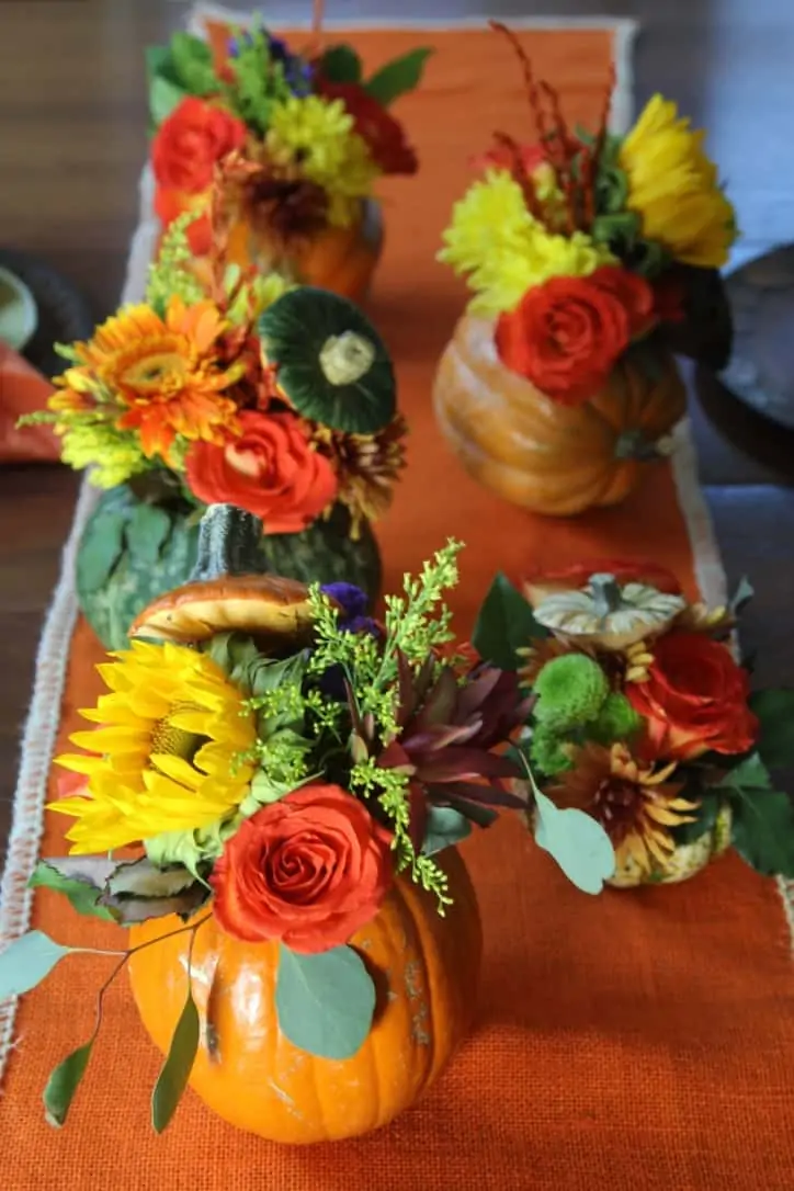 A Thanksgiving table set with real pumpkins carved out and filled with flower as centerpieces.